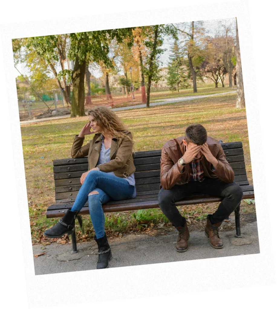 Man and woman sit on a park bench facing away from each other with their heads in their hands after an argument.