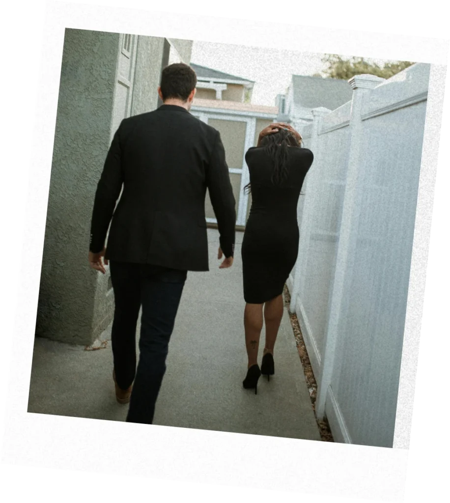 Man and woman in formal clothes walk down a narrow walkway, the woman holding her head in frustration