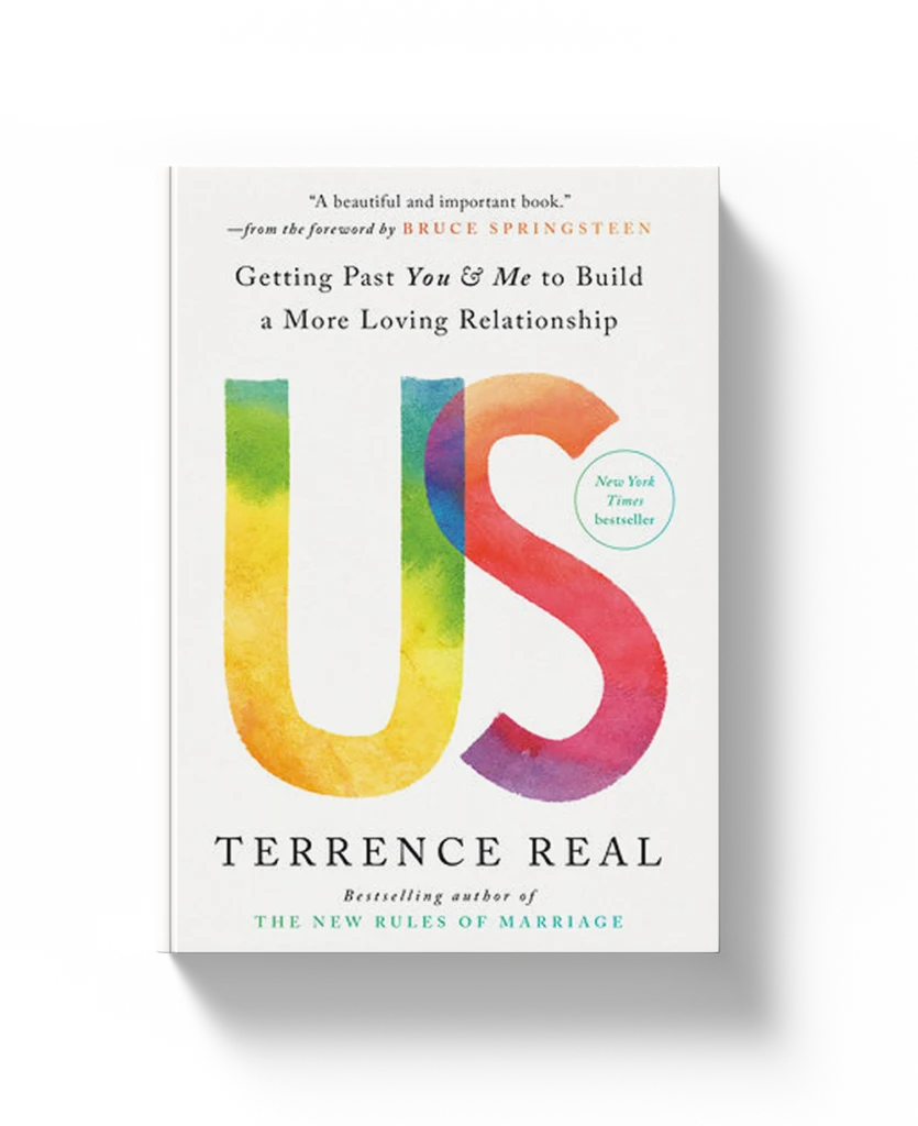 A demonstration of the physical book Us: Getting Past You and Me to Build a More Loving Relationship by Terry Real, with a white finish and large US lettering in colored watercolor.