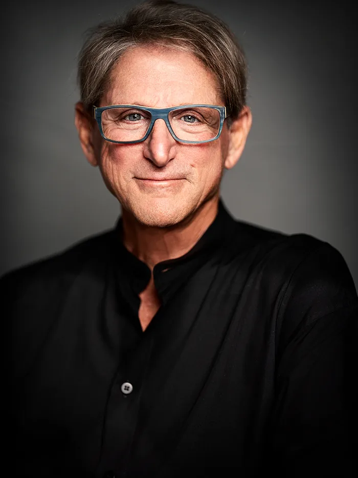 Studio portrait of Terry Real in a black shirt and blue glasses